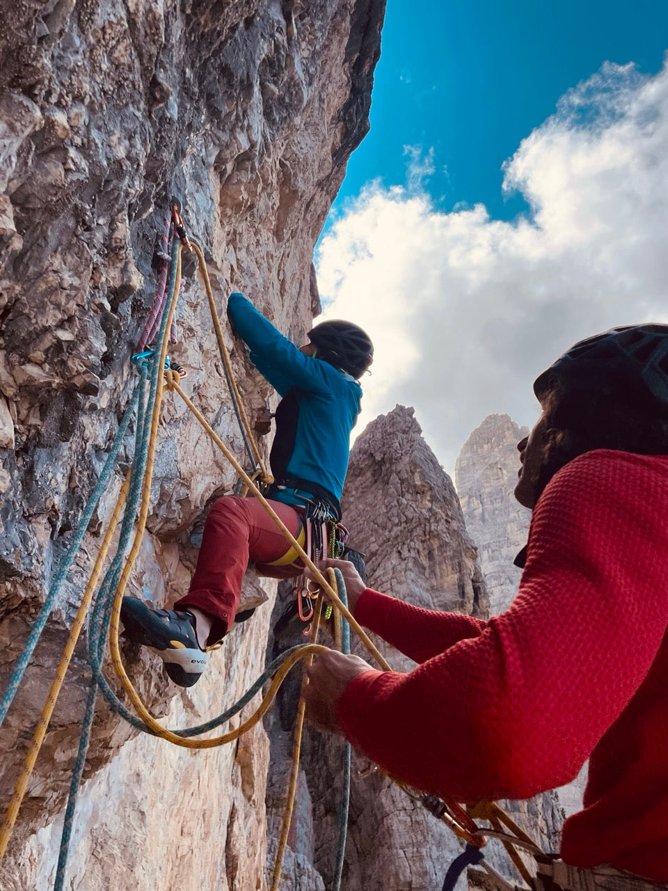 Two climbers on a rocky mountain face with one climbing and the other supporting them.