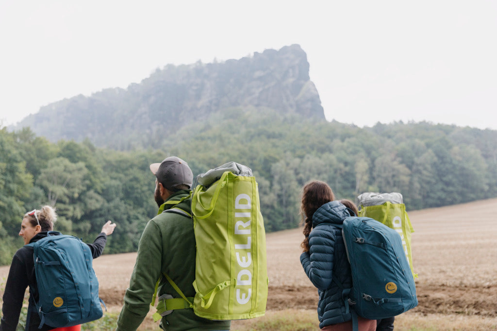 People with backpacks walking through a field with mountains in the background