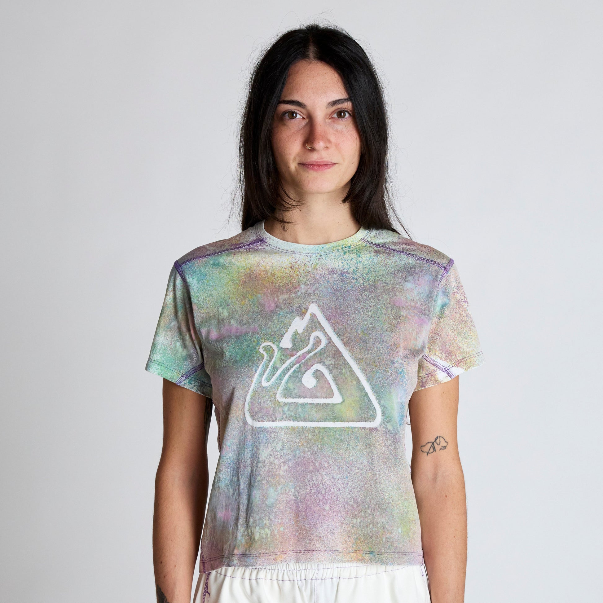 Person wearing a tie-dye t-shirt with a logo on a plain background